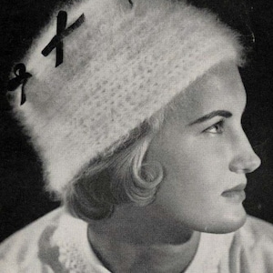 May include: A white crocheted hat with black ribbon bows on top. The hat is worn by a person with short, curly hair.