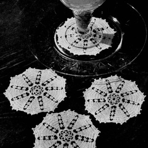 May include: Four white crocheted doilies with a delicate floral design. The doilies are arranged on a dark surface.