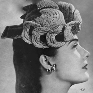 May include: A black and white photo of a woman wearing a large, crocheted hat with a unique, swirling design. The hat is made of thick, textured yarn and covers most of her head. The woman is looking to the side, and her face is partially obscured by the hat.