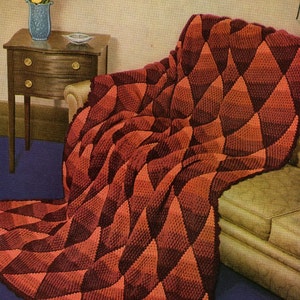 May include: A crocheted throw blanket with a diamond pattern in shades of red and orange. The blanket is draped over a sofa in a living room setting.