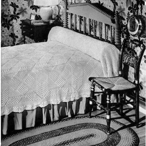 May include: A black and white photo of a bedroom with a bed, a nightstand, a lamp, a chair, and a rug. The bed has a white crocheted bedspread and a white crocheted rug. The nightstand has a lamp with a white shade and a book on top. The chair is made of wood and has a woven seat. The rug is oval shaped and has a braided design.