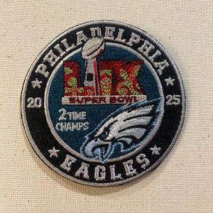 May include: Embroidered patch featuring the Philadelphia Eagles logo and text. The patch is circular, with a teal and black border. It includes the words "Philadelphia Eagles", "Super Bowl", and "2 Time Champs". The patch also features the Super Bowl trophy.