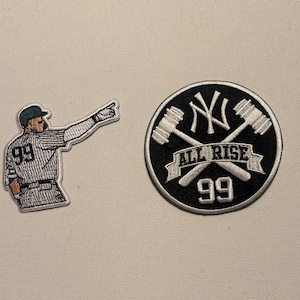 May include: Two embroidered patches. One depicts a baseball player in a pinstripe uniform, pointing. The other is a black circle with the text "ALL RISE" and the number "99", with crossed baseball bats and the NY logo.