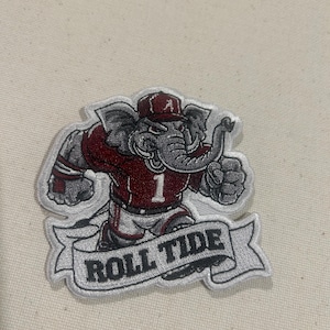 May include: Embroidered patch featuring an elephant mascot in a maroon jersey with the number 1. The elephant wears a cap with the letter "A" and the words "ROLL TIDE" are displayed on a banner below the elephant.