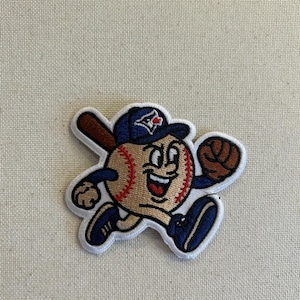 May include: Embroidered patch featuring a baseball character with a smiling face, wearing a blue baseball cap with a red maple leaf logo. The baseball is tan with red stitching, and the character is holding a brown bat and a brown baseball glove.