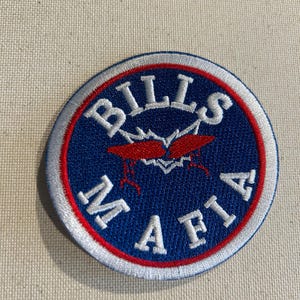 May include: A circular patch with the words "BILLS MAFIA" in white lettering on a blue background. The patch has a red and white border and features a red graphic in the center.