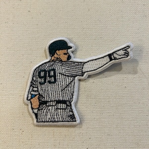 May include: Embroidered patch featuring a baseball player in a pinstriped uniform, pointing to the right. The player wears a cap and the number 99 is visible on the back of the jersey. The patch has a white border.