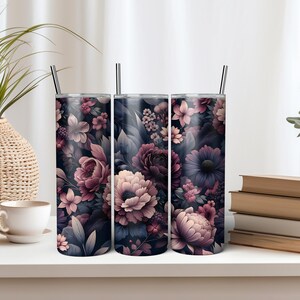 Puede incluir: Tres vasos de acero inoxidable con dise&ntilde;os florales. Los vasos presentan un fondo oscuro con flores rosas, moradas y blancas. Cada vaso tiene una pajita plateada. Los vasos se exhiben sobre una superficie blanca.
