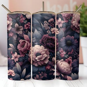 Puede incluir: Tres vasos de acero inoxidable con tem&aacute;tica floral con tapas y pajitas. Los vasos presentan un fondo azul marino oscuro con un patr&oacute;n de flores y hojas rosas, moradas y blancas. Los vasos son cil&iacute;ndricos y tienen un borde dorado met&aacute;lico.