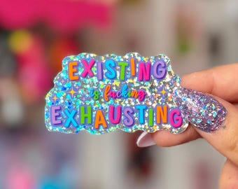 May include: A glittery sticker with the text "EXISTING is f*cking EXHAUSTING" in colorful bubble letters. The sticker has a silver glitter background and a wavy outline. The image is a close-up shot.
