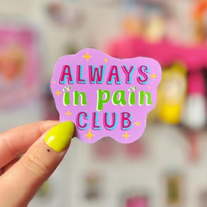 May include: A sticker with the text "ALWAYS in pain CLUB" in a playful font. The sticker has a light purple background with yellow star accents and a turquoise border. The words "ALWAYS" and "CLUB" are in red, and "in pain" is in green.