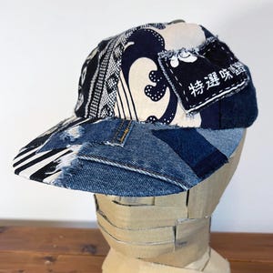 May include: A black, white, and blue denim baseball cap with a patchwork design. The cap has a white fabric panel with a black and white pattern and a blue fabric panel with Japanese text that reads "Special Delivery".