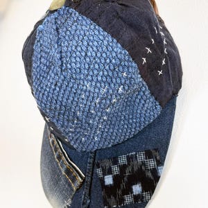 May include: A blue denim baseball cap with a patchwork design. The cap is made of different shades of blue denim and has a black and white checkered patch on the side.