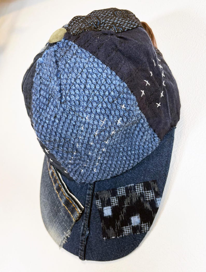 May include: A blue denim baseball cap with a patchwork design. The cap is made of different shades of blue denim and has a black and white checkered patch on the side.