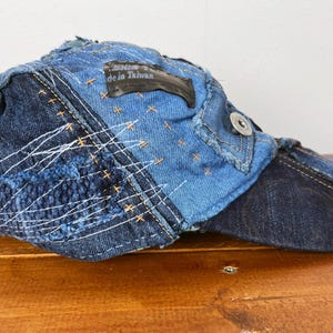 Op de afbeelding: Een blauwe denim baseballcap met een patchwork ontwerp en een zwart label met de tekst "Made in Taiwan".