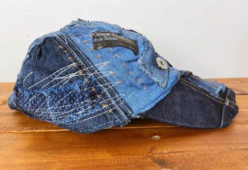 Op de afbeelding: Een blauwe denim baseballcap met een patchwork ontwerp en een zwart label met de tekst "Made in Taiwan".