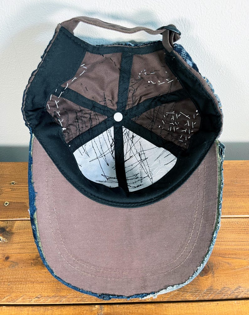 May include: A blue denim baseball cap with a brown fabric lining and a white button on the top. The cap has a distressed look with frayed edges.