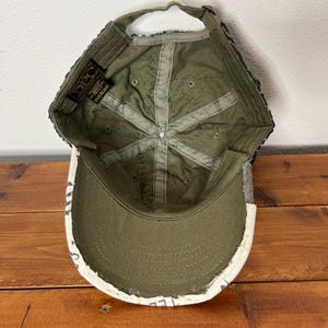 May include: An olive green baseball cap shown from the interior perspective, featuring a structured crown with internal fabric seams, a curved brim, and an adjustable strap at the back. A black DPC brand label is stitched inside the crown.