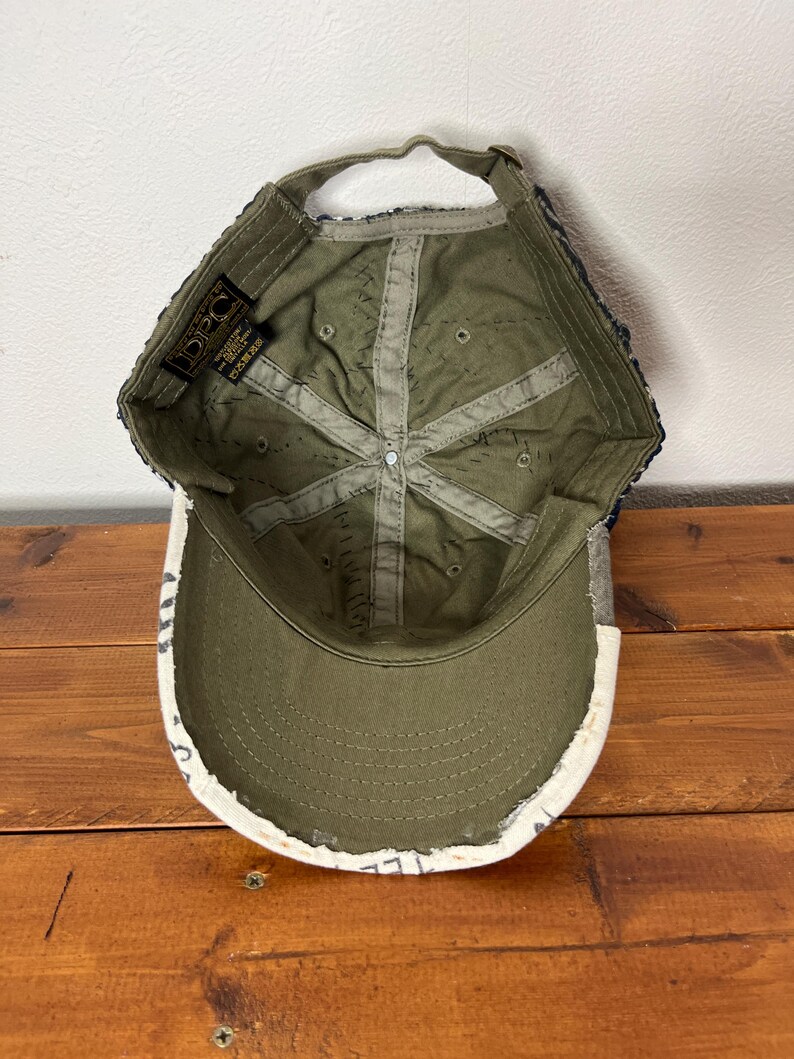 May include: An olive green baseball cap shown from the interior perspective, featuring a structured crown with internal fabric seams, a curved brim, and an adjustable strap at the back. A black DPC brand label is stitched inside the crown.