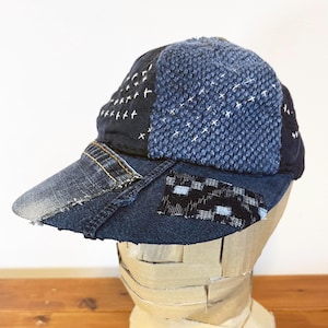 May include: A blue denim baseball cap with a patchwork design. The cap is made of different shades of blue denim and has a variety of stitching details. The brim of the cap is also made of denim and has a frayed edge.