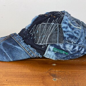 Op de afbeelding: Een blauwe denim baseballcap met een patchwork ontwerp. De cap is gemaakt van verschillende stukken denim die aan elkaar zijn genaaid, waardoor een unieke en textuurrijke look ontstaat.
