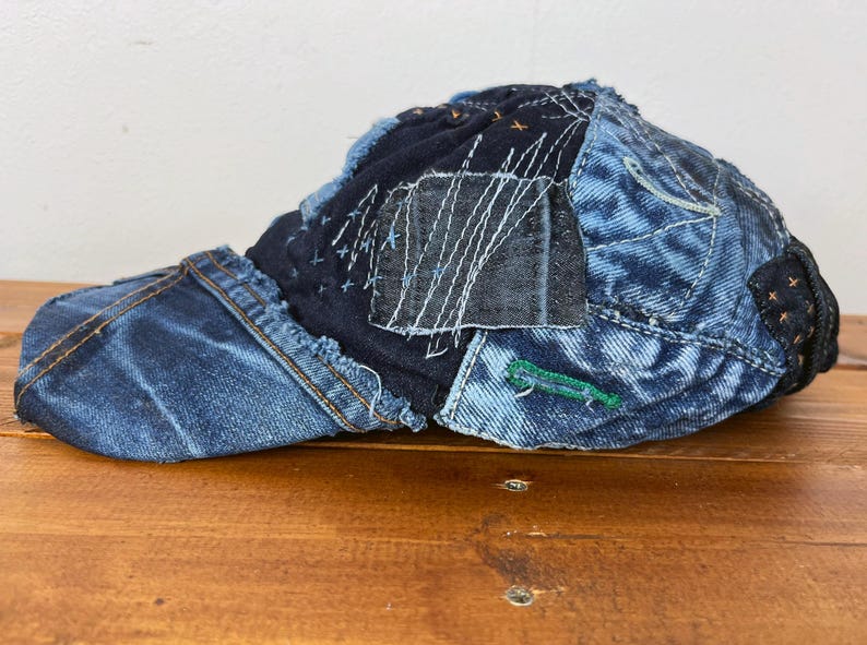 Op de afbeelding: Een blauwe denim baseballcap met een patchwork ontwerp. De cap is gemaakt van verschillende stukken denim die aan elkaar zijn genaaid, waardoor een unieke en textuurrijke look ontstaat.