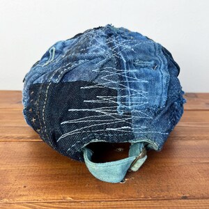 Op de afbeelding: Een blauwe denim baseballcap met een patchwork ontwerp. De cap is gemaakt van verschillende tinten blauw denim en heeft witte stiksels. De cap heeft een bandje aan de achterkant om de pasvorm aan te passen.