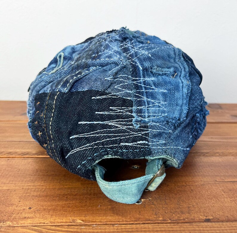 Op de afbeelding: Een blauwe denim baseballcap met een patchwork ontwerp. De cap is gemaakt van verschillende tinten blauw denim en heeft witte stiksels. De cap heeft een bandje aan de achterkant om de pasvorm aan te passen.