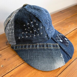 May include: A blue denim and patchwork baseball cap with white stitching. The cap is made of different fabrics and has a distressed look.