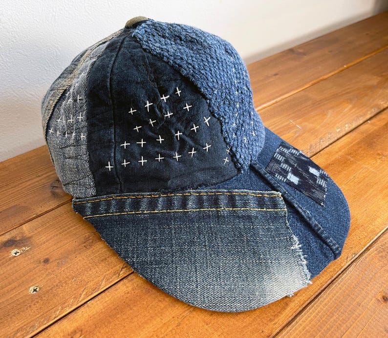 May include: A blue denim and patchwork baseball cap with white stitching. The cap is made of different fabrics and has a distressed look.