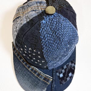 May include: A blue denim baseball cap with a patchwork design. The cap is made of different shades of blue denim and has a small brown button on top.