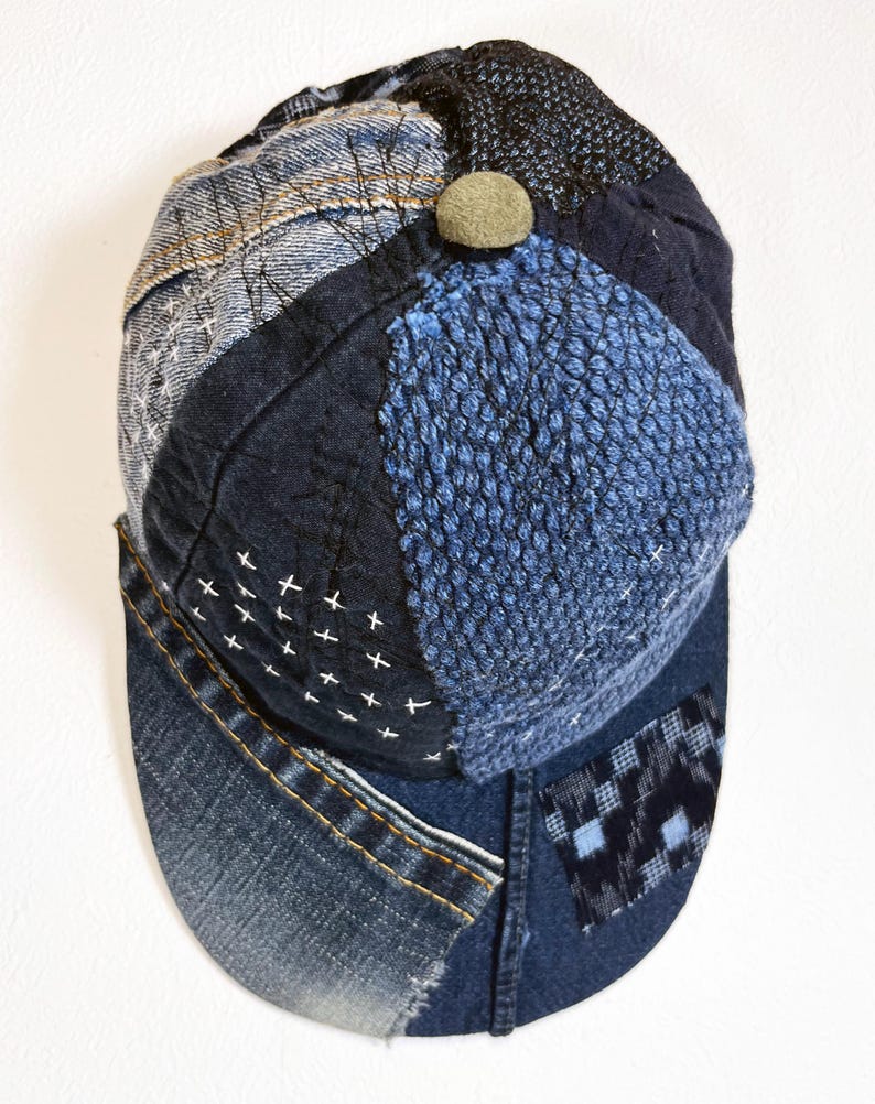 May include: A blue denim baseball cap with a patchwork design. The cap is made of different shades of blue denim and has a small brown button on top.