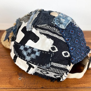 Op de afbeelding: Een zwarte, blauwe en witte patchwork baseballcap met een rafelige rand. De cap is gemaakt van verschillende stoffen en heeft een unieke, handgemaakte uitstraling.