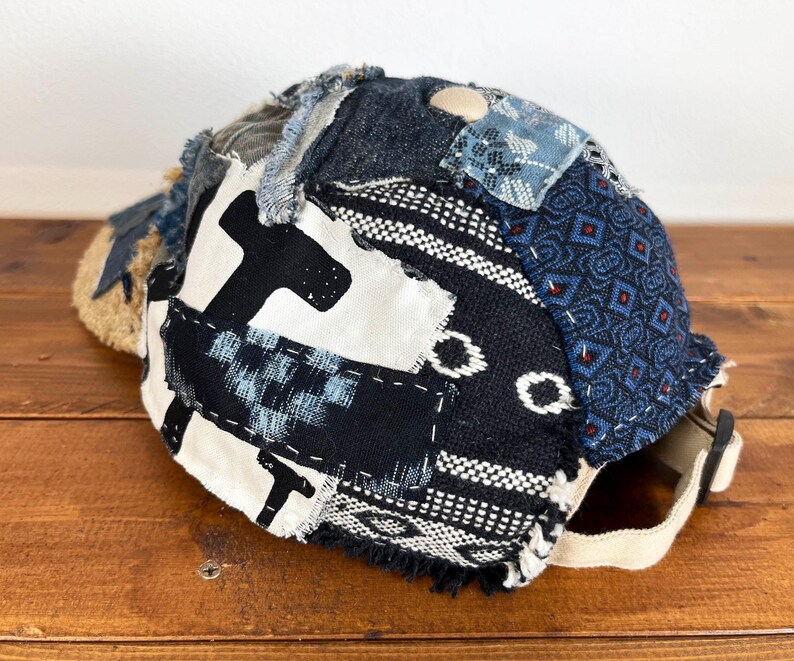 Op de afbeelding: Een zwarte, blauwe en witte patchwork baseballcap met een rafelige rand. De cap is gemaakt van verschillende stoffen en heeft een unieke, handgemaakte uitstraling.