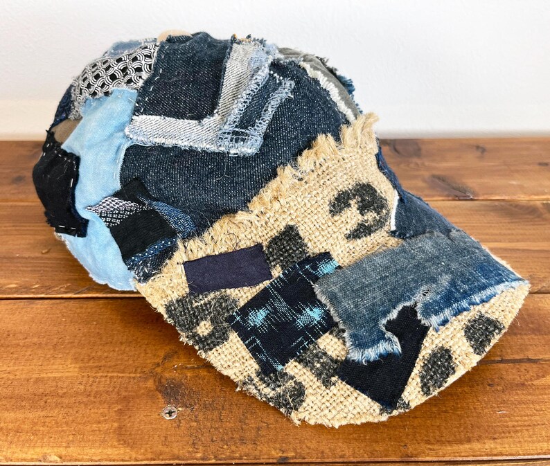 Op de afbeelding: Een blauwe en bruine patchwork baseballcap met rafelige randen. De cap is gemaakt van denim en jute stof.