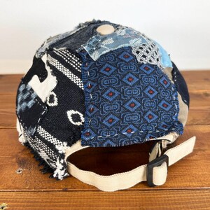 Op de afbeelding: Een zwarte en blauwe patchwork baseballcap met een beige band. De cap is gemaakt van verschillende stoffen met verschillende patronen, waaronder geometrische ontwerpen en bloemmotieven.