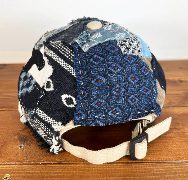 Op de afbeelding: Een zwarte en blauwe patchwork baseballcap met een beige band. De cap is gemaakt van verschillende stoffen met verschillende patronen, waaronder geometrische ontwerpen en bloemmotieven.