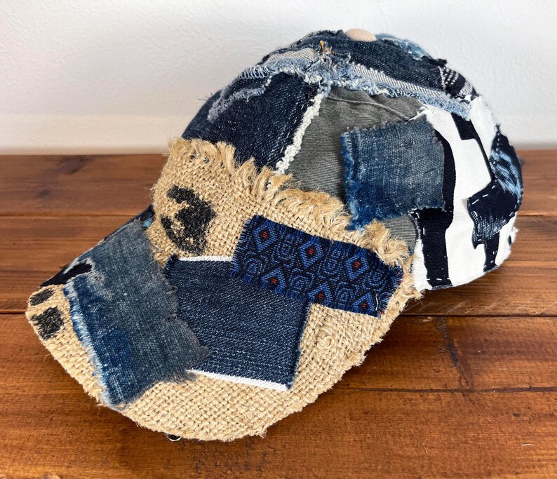 Op de afbeelding: Een bruine, beige en blauwe patchwork baseballcap met een rafelige rand. De cap is gemaakt van verschillende stoffen, waaronder denim, jute en canvas.