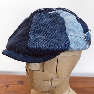 May include: A blue and black patchwork newsboy cap made from denim and knit fabric. The cap has a slightly curved brim and a crown with a textured pattern.