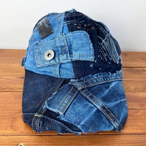 Op de afbeelding: Een blauwe denim baseballcap gemaakt van patchwork denim stof. De cap heeft verschillende stikdetails en een knoop bovenop.