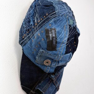 Op de afbeelding: Een blauwe denim baseballcap met een patchwork-ontwerp. De cap is gemaakt van verschillende stukken denim die aan elkaar zijn genaaid, en heeft een rafelige rand. De cap heeft een klein zwart label met de tekst "SKIN TUBE" erop.