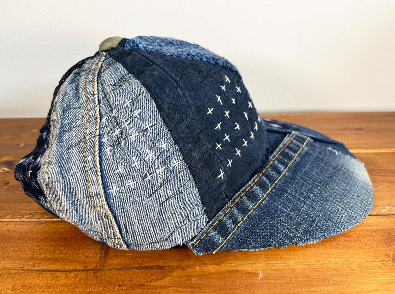May include: A blue denim baseball cap with a patchwork design. The cap is made of different shades of blue denim and features white stitching in a cross pattern.