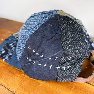 May include: A blue and black patchwork baseball cap with white stitching. The cap is made of different fabrics and has a unique, handmade look.