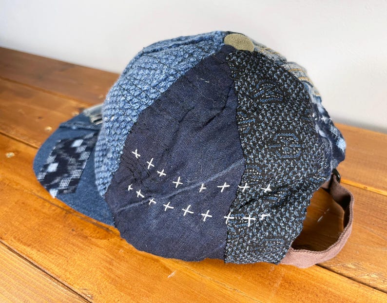 May include: A blue and black patchwork baseball cap with white stitching. The cap is made of different fabrics and has a unique, handmade look.