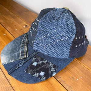 May include: A blue denim baseball cap with a patchwork design. The cap is made of different shades of blue denim and has a stitched pattern on the top.