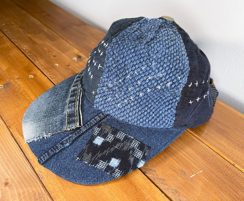 May include: A blue denim baseball cap with a patchwork design. The cap is made of different shades of blue denim and has a stitched pattern on the top.