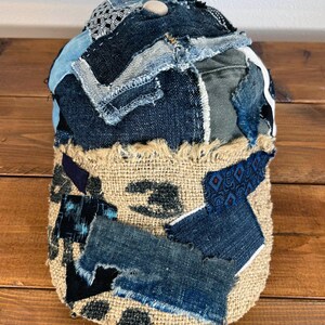 Op de afbeelding: Een baseballpet van denim en jute met een patchwork-ontwerp. De pet is gemaakt van verschillende tinten blauw denim en heeft een gescheurde jute rand.