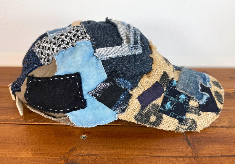 Op de afbeelding: Een bruine, blauwe en zwarte patchwork baseballcap met een gebogen klep. De cap is gemaakt van verschillende stoffen, waaronder denim, jute en katoen.