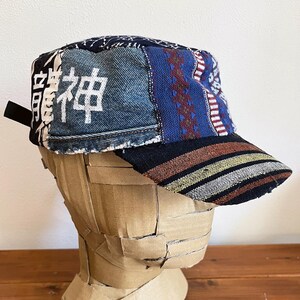 May include: A blue and black patchwork baseball cap with a white embroidered kanji character on the front. The cap has a striped brim.