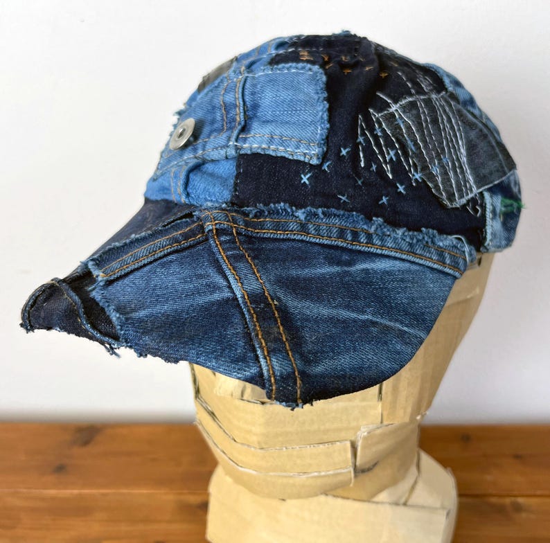 Op de afbeelding: Een blauwe denim baseballcap met een patchwork ontwerp. De cap is gemaakt van verschillende tinten blauw denim en heeft een rafelige rand.